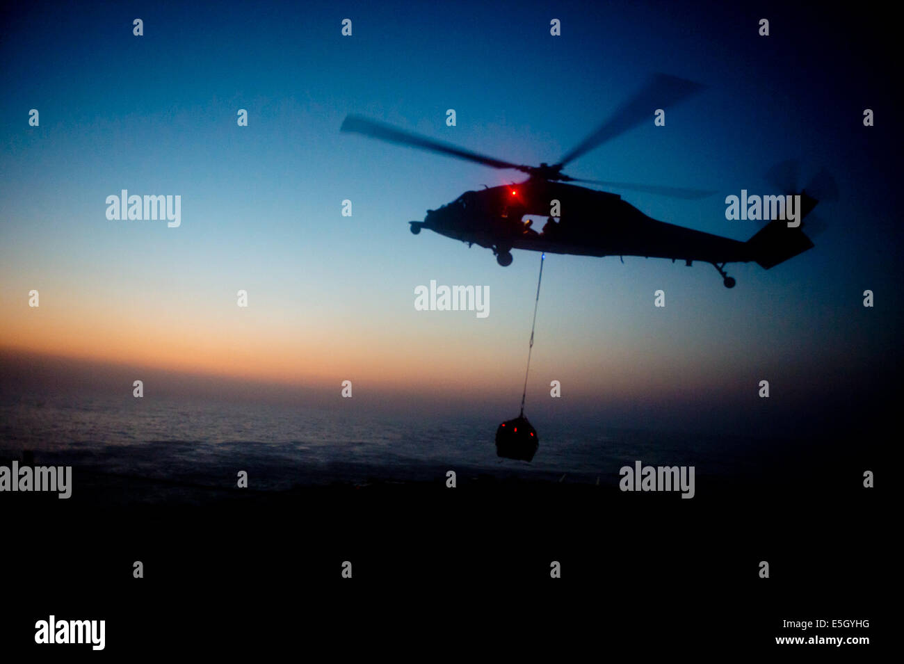 A U.S. Navy MH-60S Seahawk helicopter assigned to Helicopter Sea Combat Squadron (HSC) 26 retrieves cargo from the flight deck Stock Photo