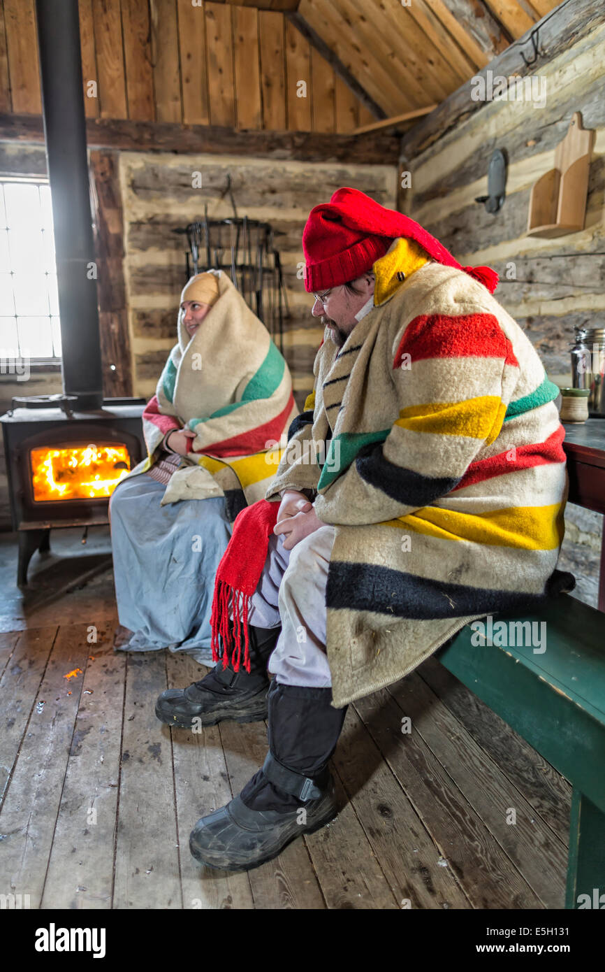 A voyageur couple keeping warm by a woodstove fire, Festival du Voyageur, Winnipeg, Manitoba, Canada Stock Photo