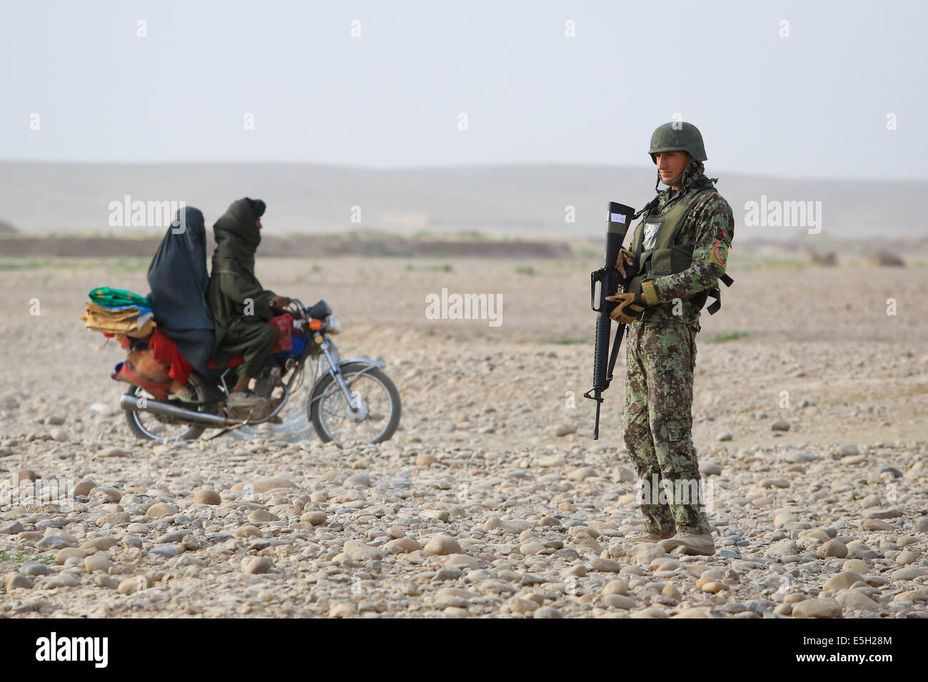 Afghan civilians ride past an Afghan National Army soldier with the 4th Tolay, 6th Kandak, 6th Brigade, 215th Corps as he provi Stock Photo