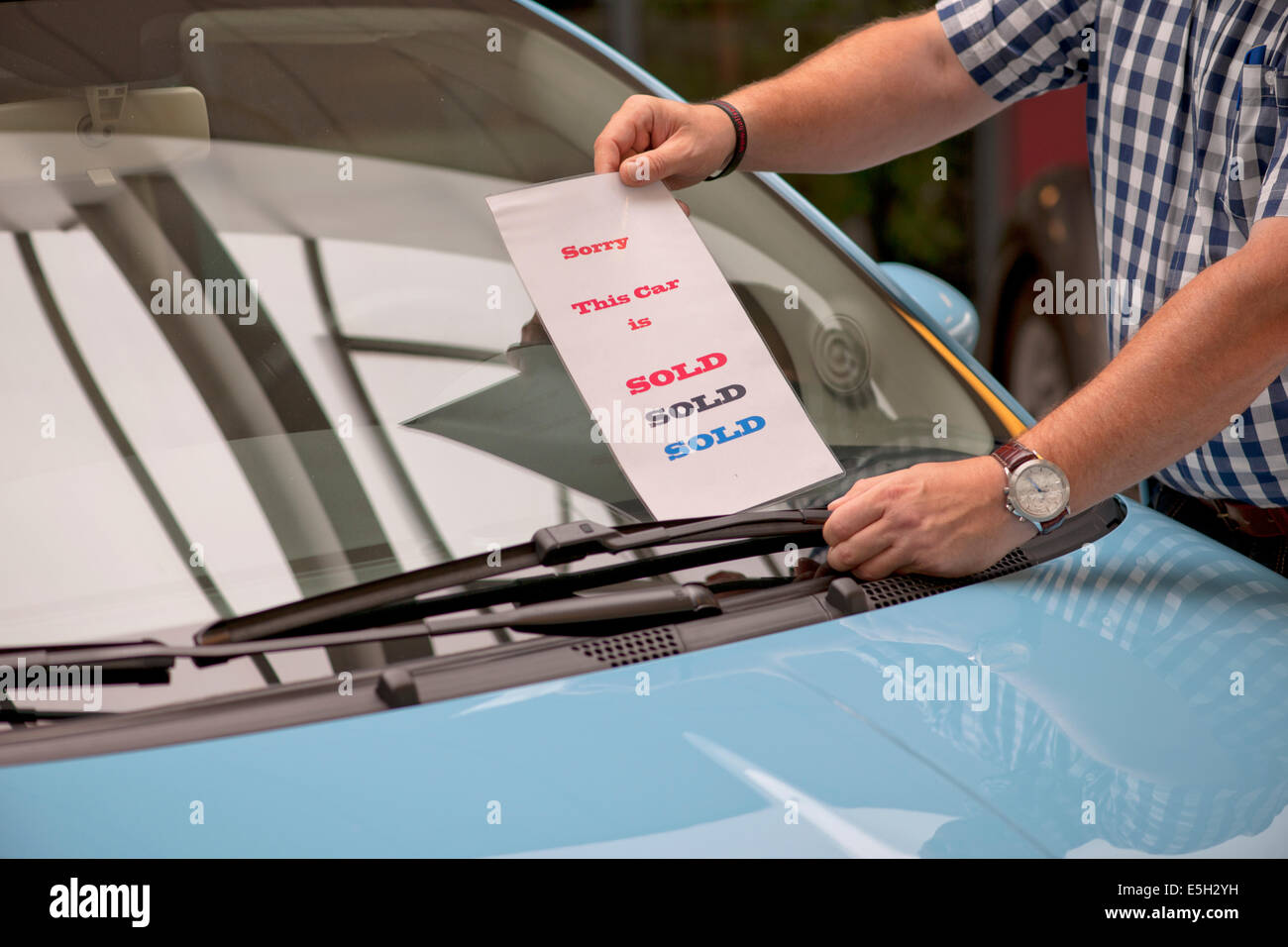 Car salesman puts a sold sign under the wiper of a car that is sold Stock Photo