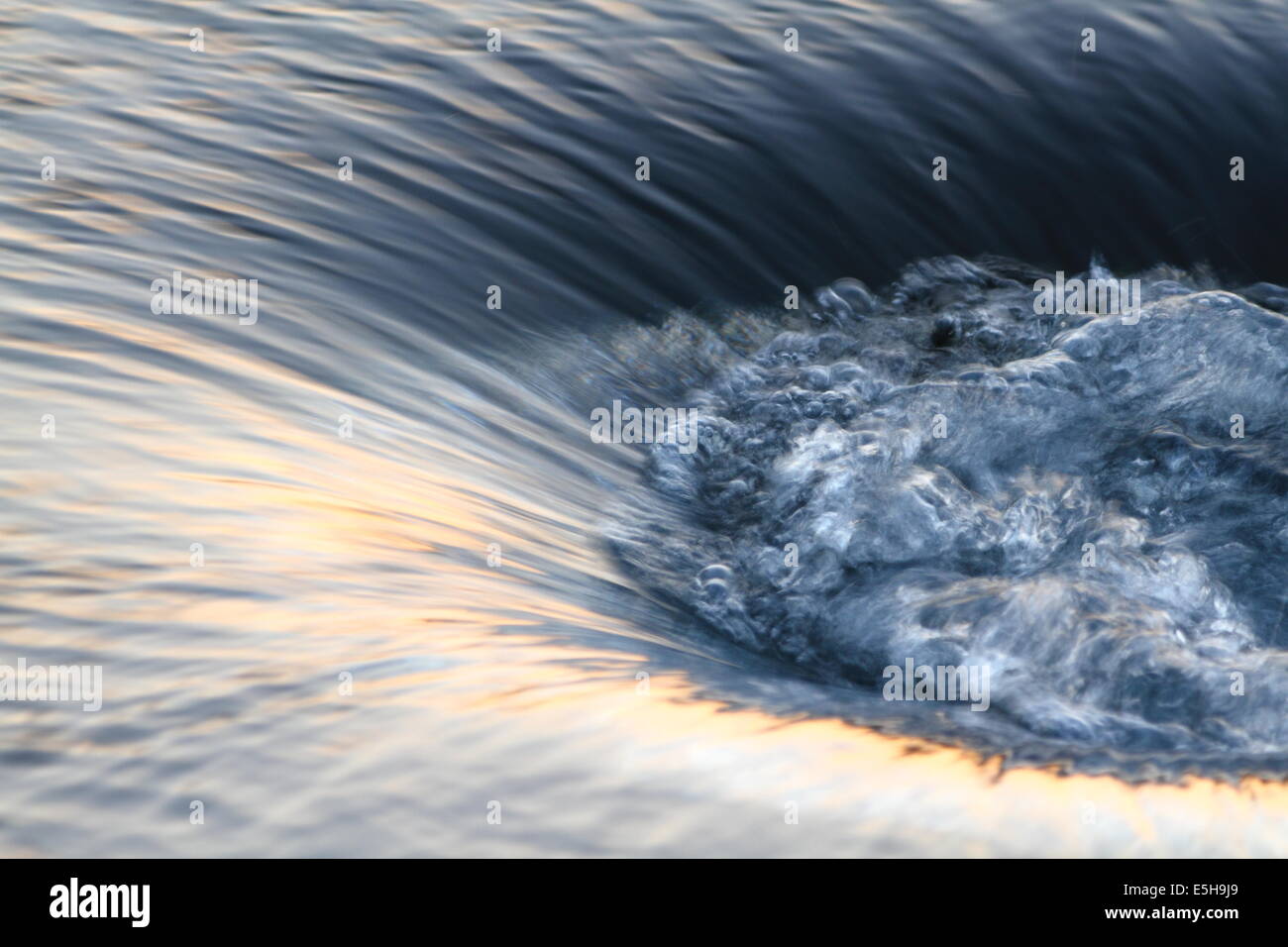 Water swirls and bubbles as it descends into a whirlpool-like funnel. Stock Photo