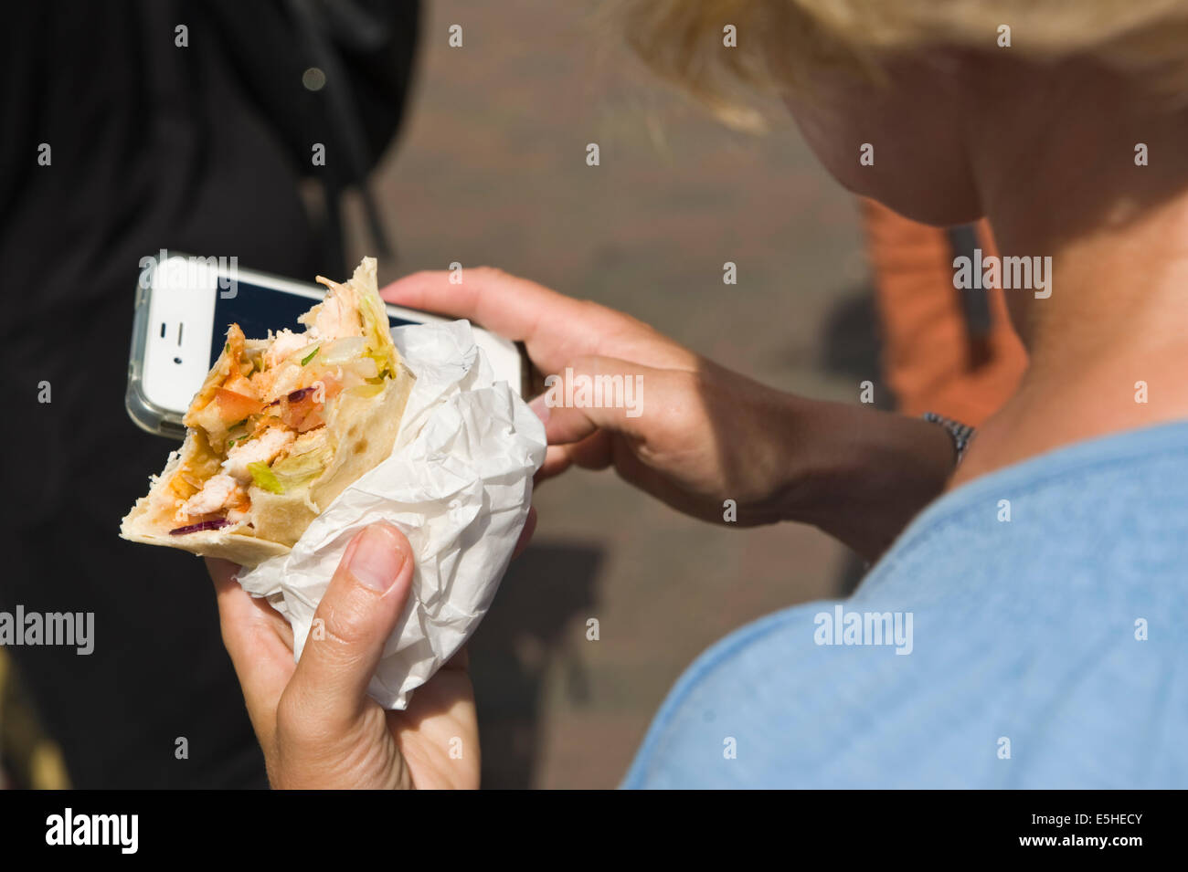 Woman using smartphone while eating a salad wrap during Oyster Festival at Whitstable Kent England UK Stock Photo