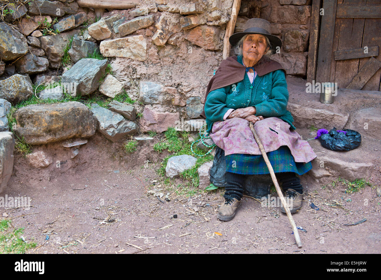 Mature Quechua Indian woman wearing a hat sitting on a stone in front of a doorway, Cordillera Huayhuash, Northern Peru, Peru Stock Photo