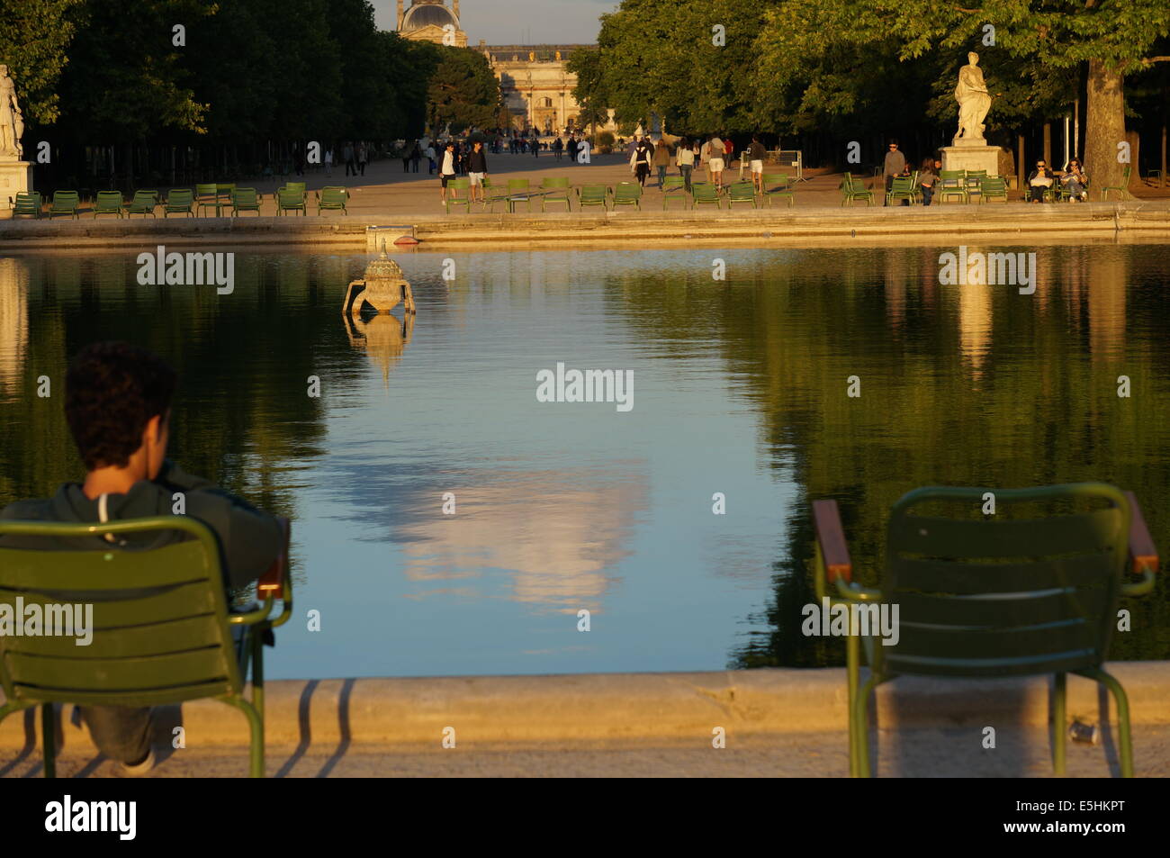 Jardin du Tuileries Garden Paris at sunset reflected in its pond with rear view of a man sitting in a chair, the other empty one Stock Photo