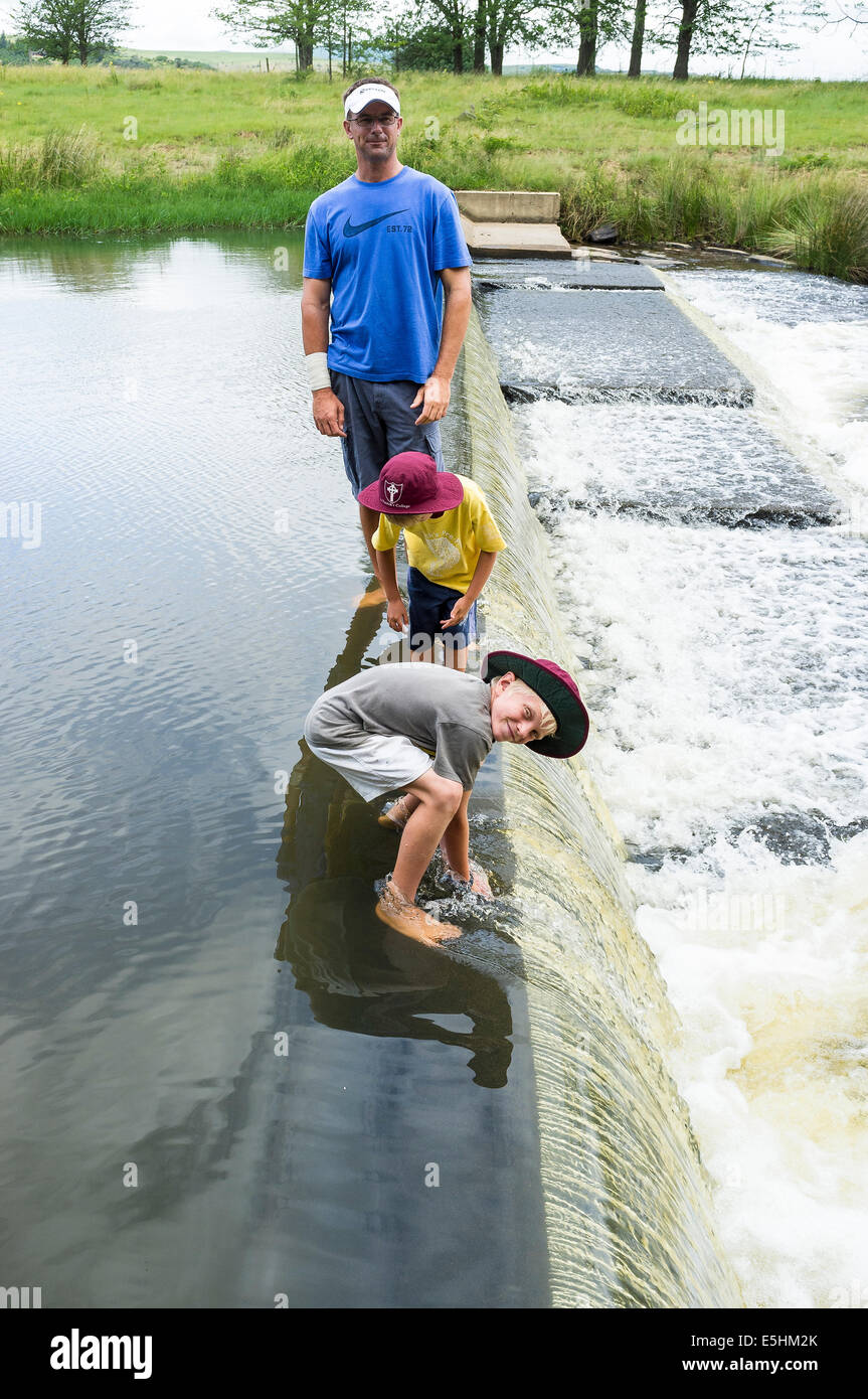 Father and sons explore river weir Stock Photo