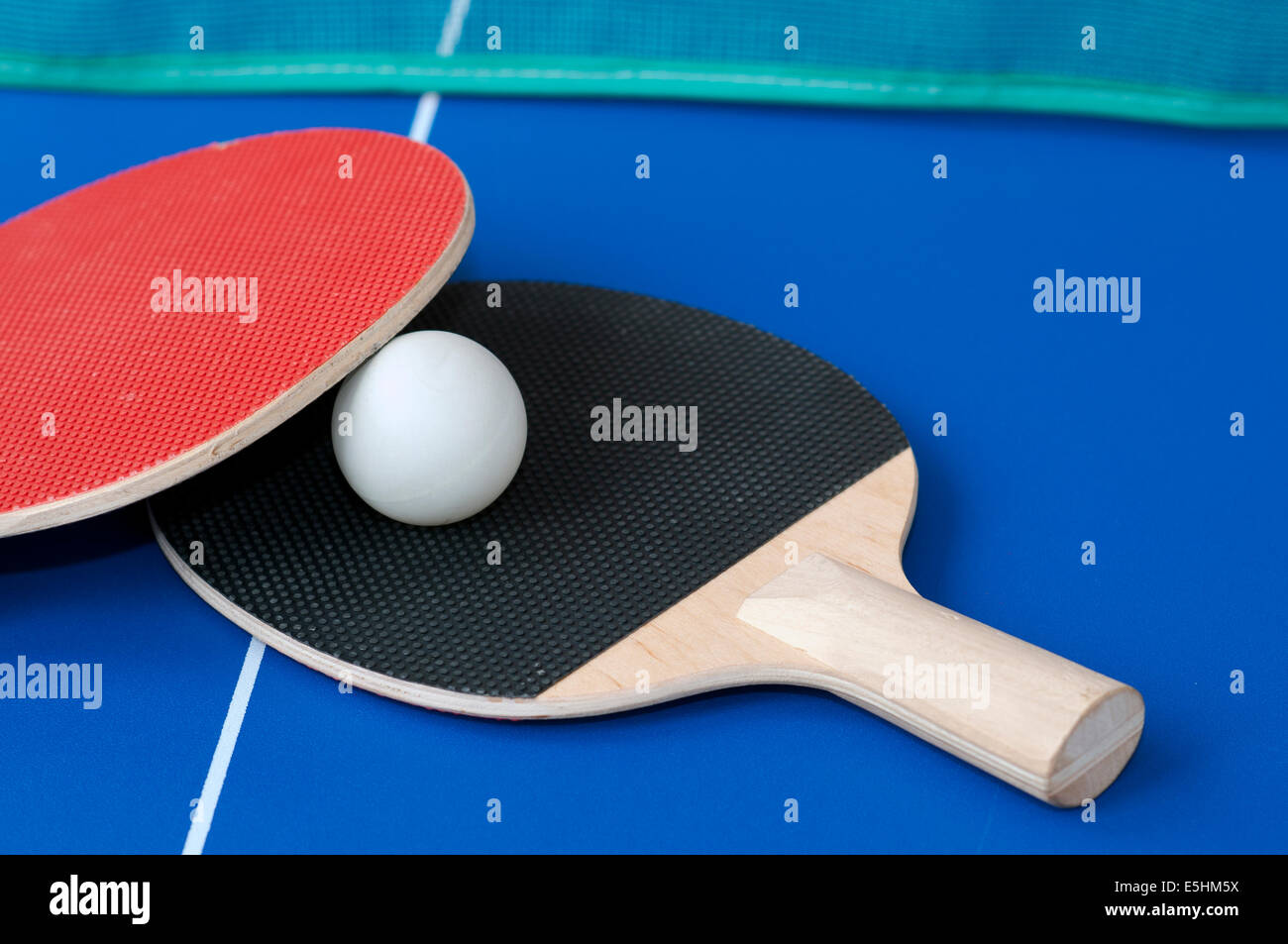 red and black table tennis bats on a blue table with green net in background Stock Photo