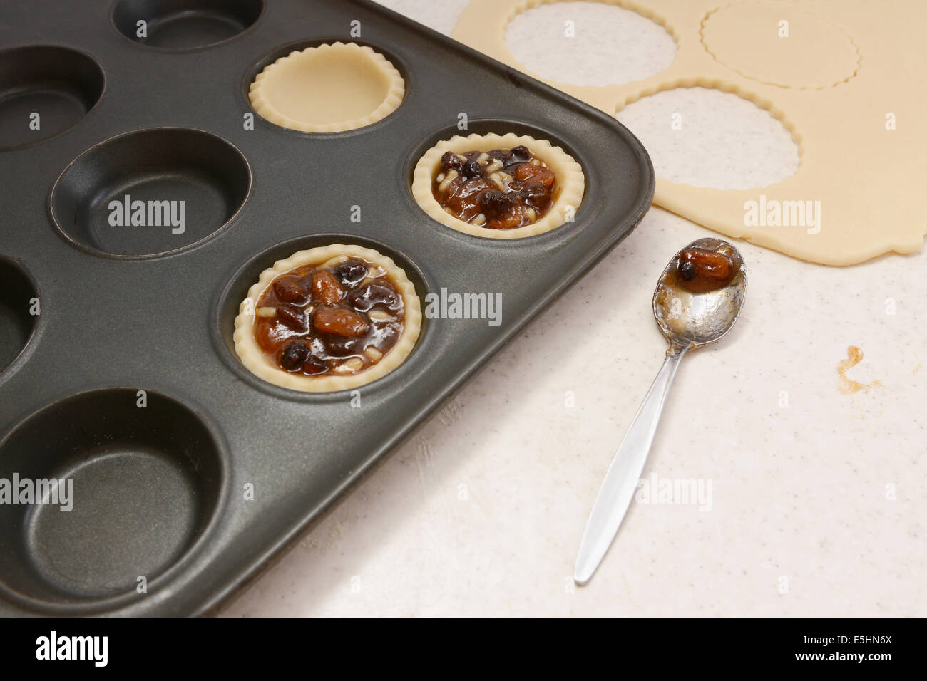 Filling pastry cases with mincemeat, with a used teaspoon on worktop