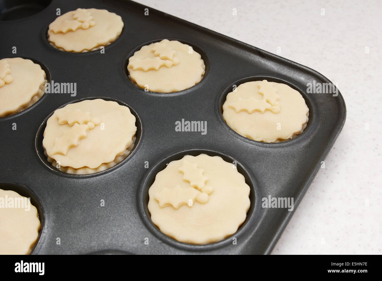 Mince pies in a bun tin ready for the oven, with pastry holly leaf