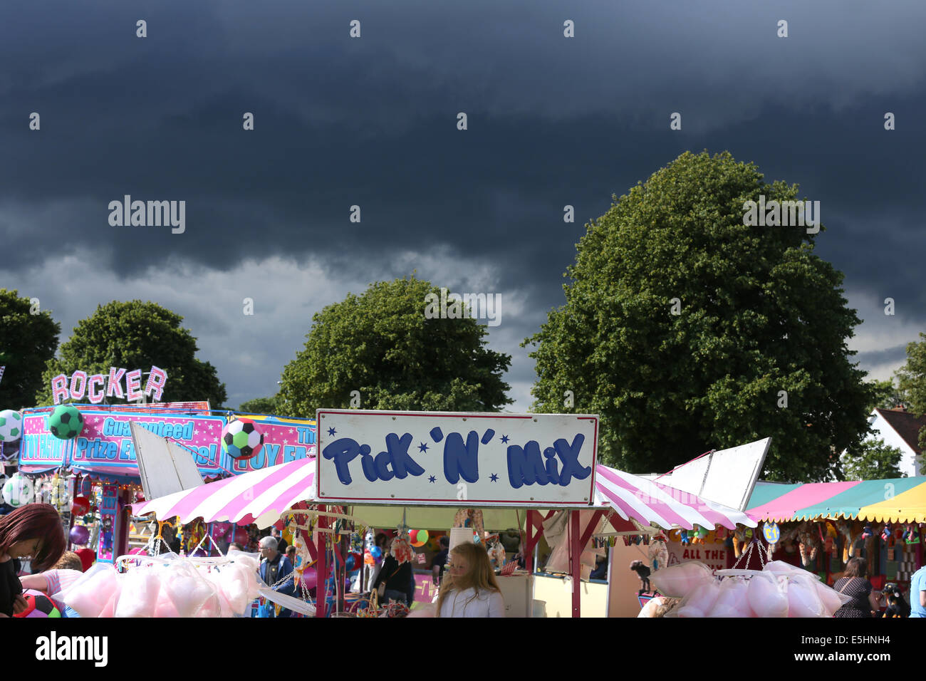 Typical British fairground scene with rides and trees with dark clouds gathering behind it Stock Photo