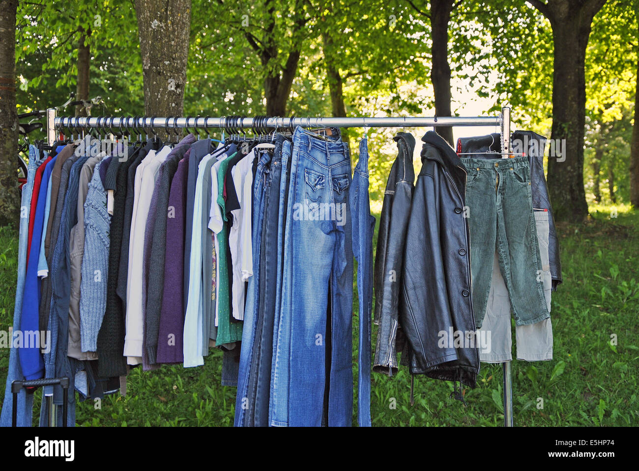 old, worn clothes on a hanging rail in a second hand market, outdoors, close up Stock Photo