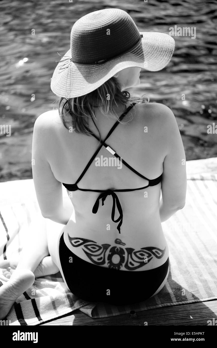 BW back of women with hat on by water and a tribal tattoo on back Stock Photo
