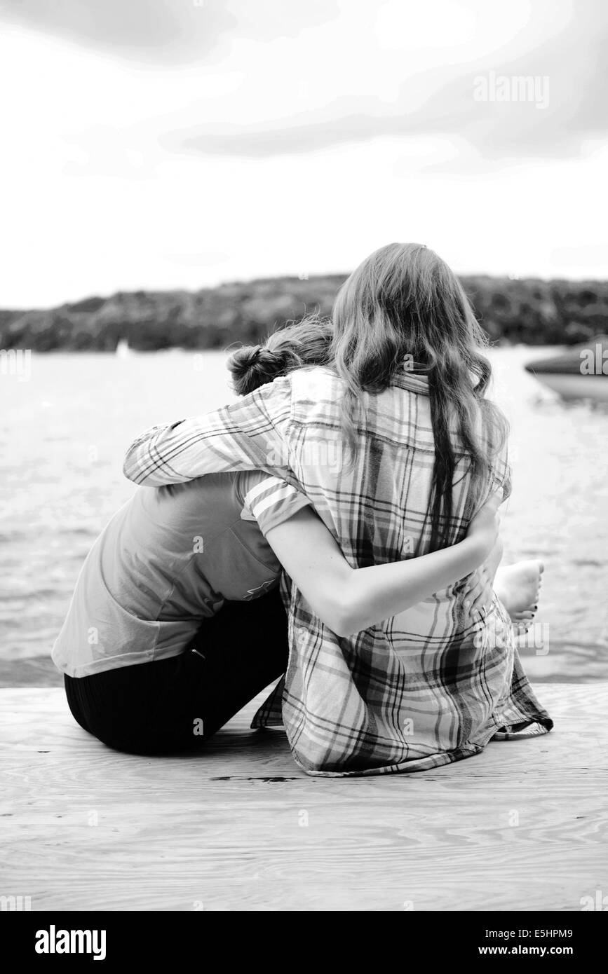 sisters hug by lake on dock in black and white Stock Photo