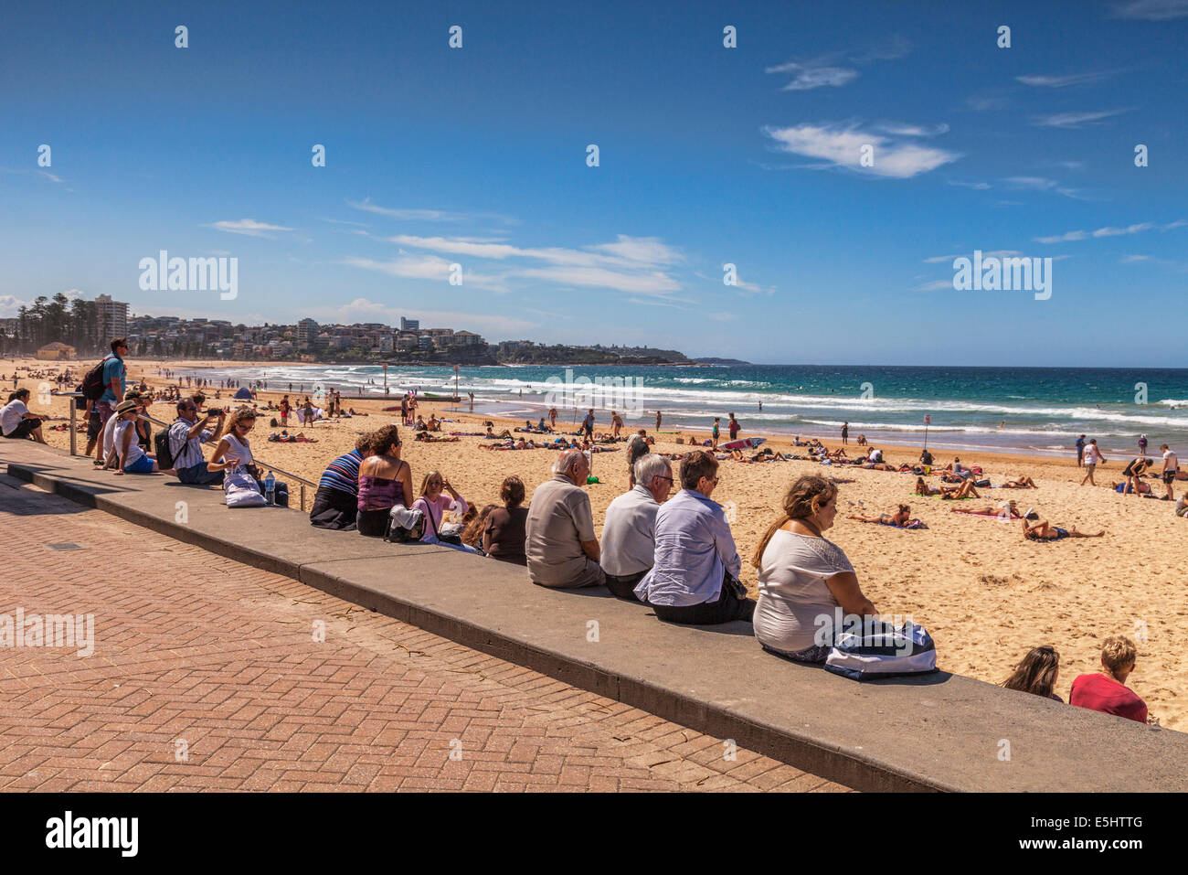 People sitting in a row on a wall and looking out over Manly Beach, Sydney, Australia. Stock Photo