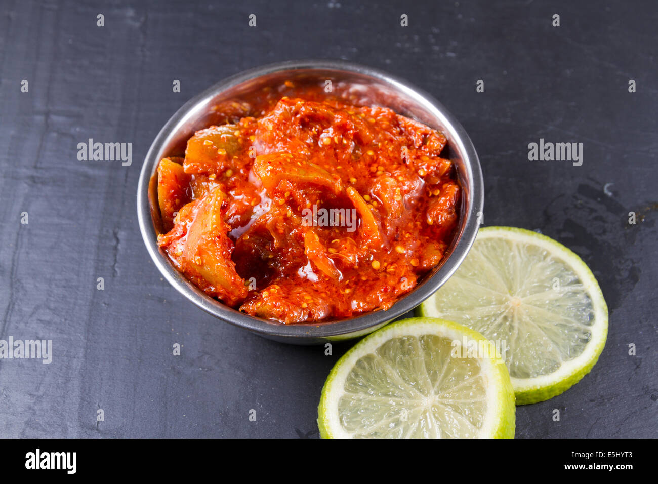 Indian chutney lime pickle in metal bowl. Accompaniment for poppadoms. Two lime slices. Stock Photo