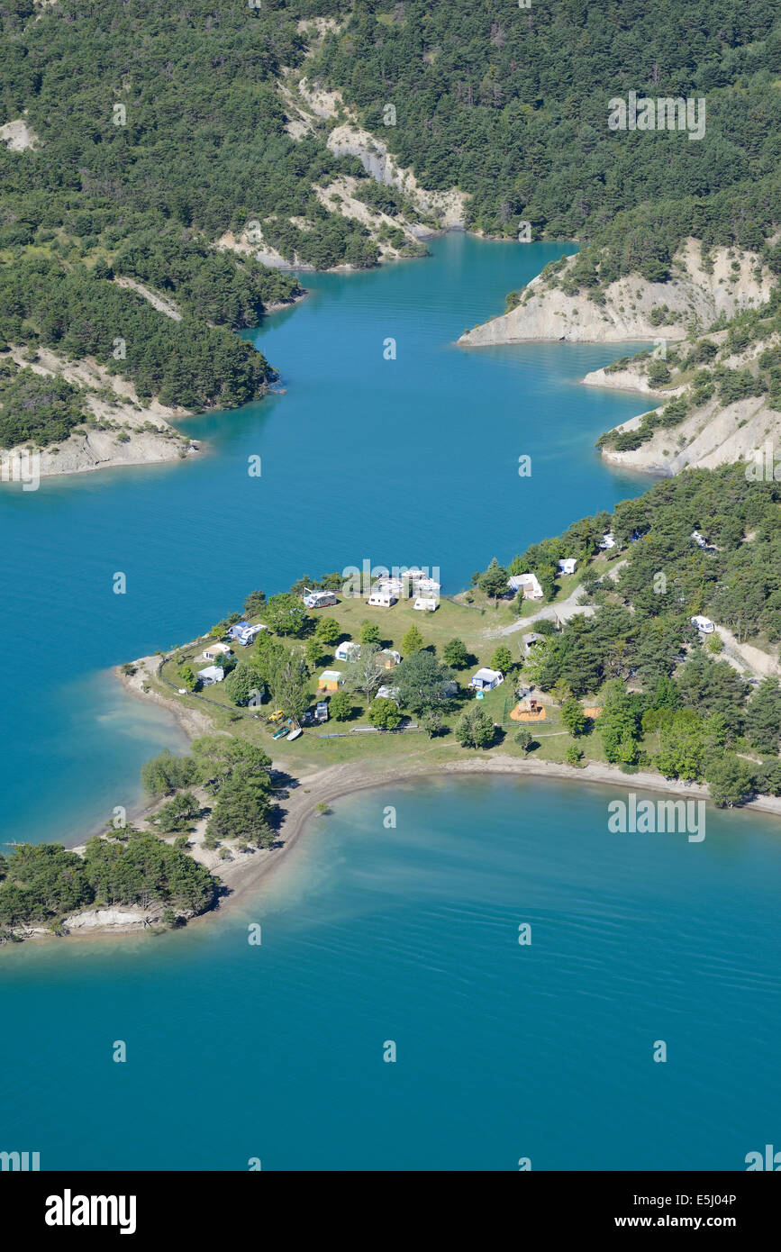 AERIAL VIEW. Campground in an idyllic setting on the lakeshore of Lake Serre-Ponçon. Chorges, Hautes-Alpes, France. Stock Photo