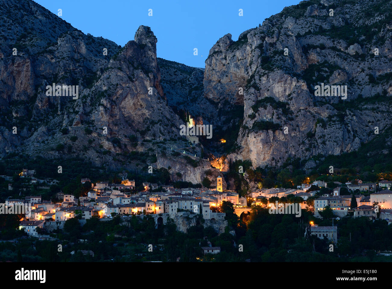Provencal village at the foot of a massive limestone cliff at twilight. Moustiers-Sainte-Marie, Alpes-de-Haute-Provence, France. Stock Photo