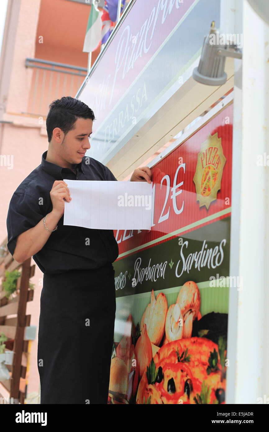 Young male waiter changing the price of the fixed price menu as part of the August price rise in the Costa Brava. Stock Photo