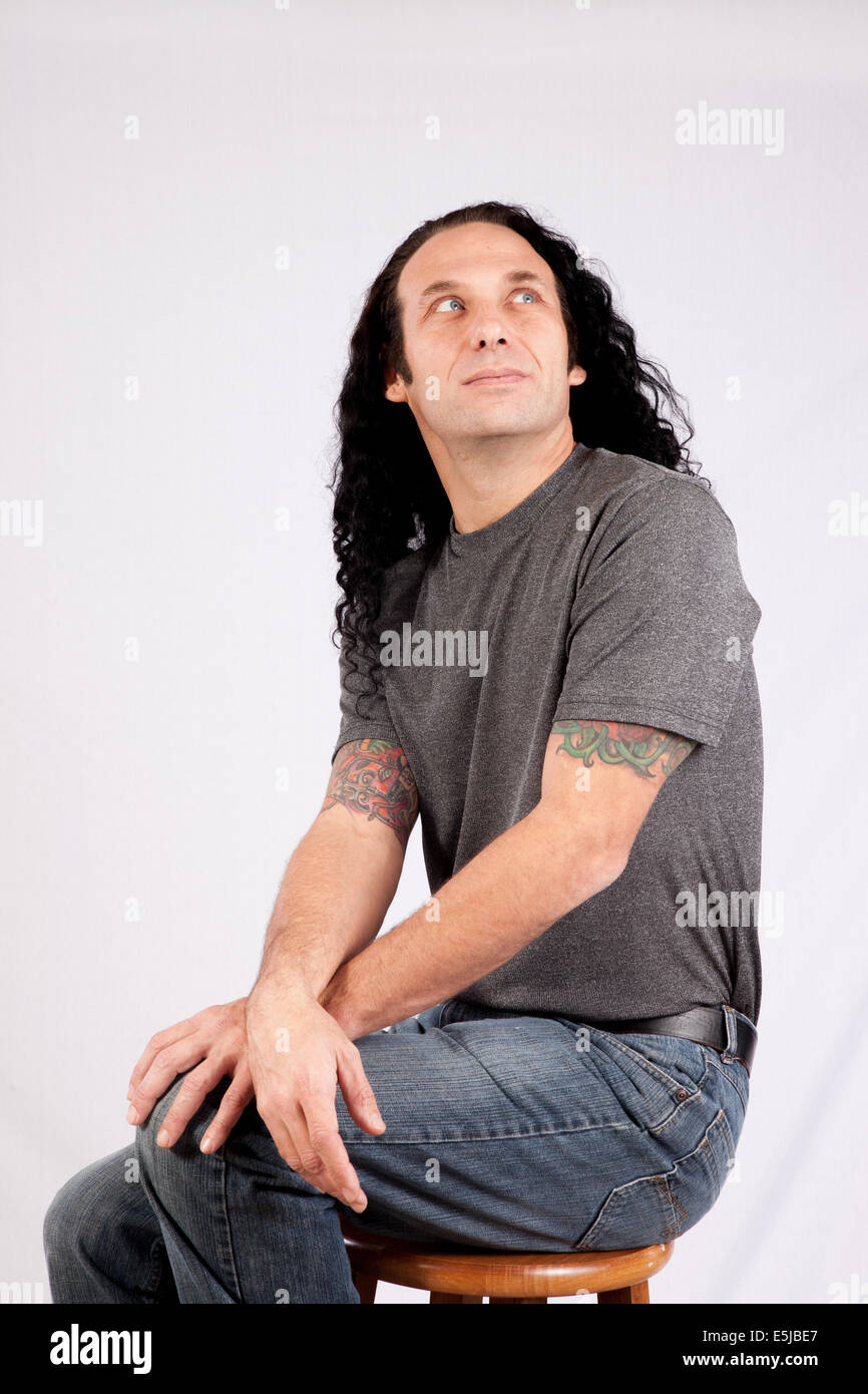 Caucasian male with long hair and gray shirt looking thoughtful Stock Photo