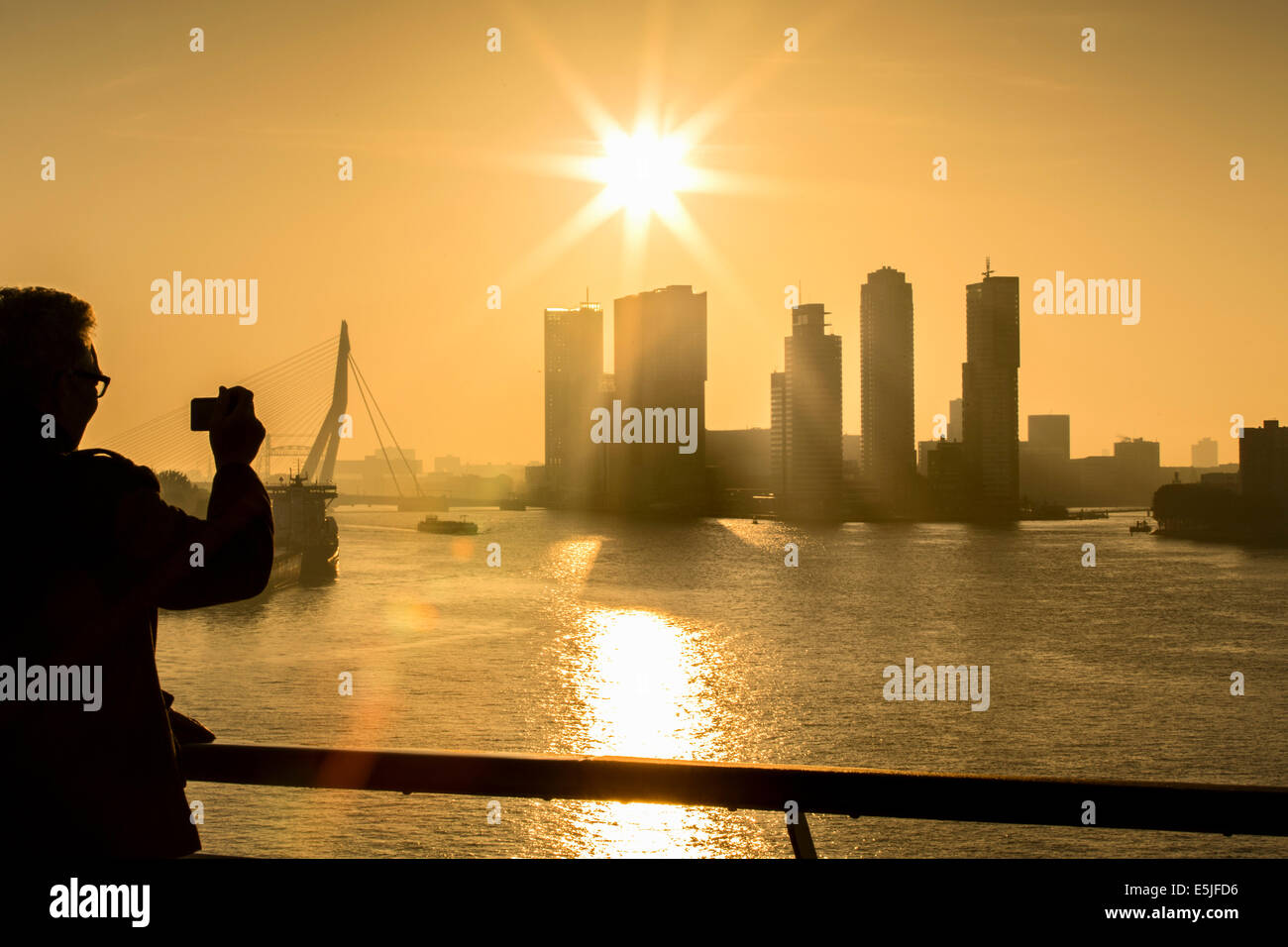 Netherlands, Rotterdam, Kop van Zuid District highrise buildings. Erasmus bridge. Sunrise. Man takes picture Stock Photo