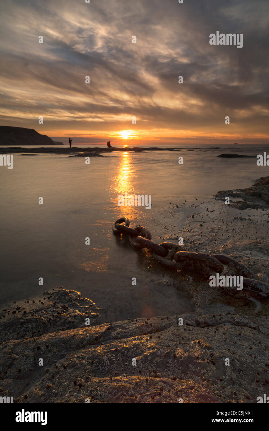 Two young men fishing on the shore at Staithes on the North Yorkshire coast at sunset in mid-summer. Stock Photo