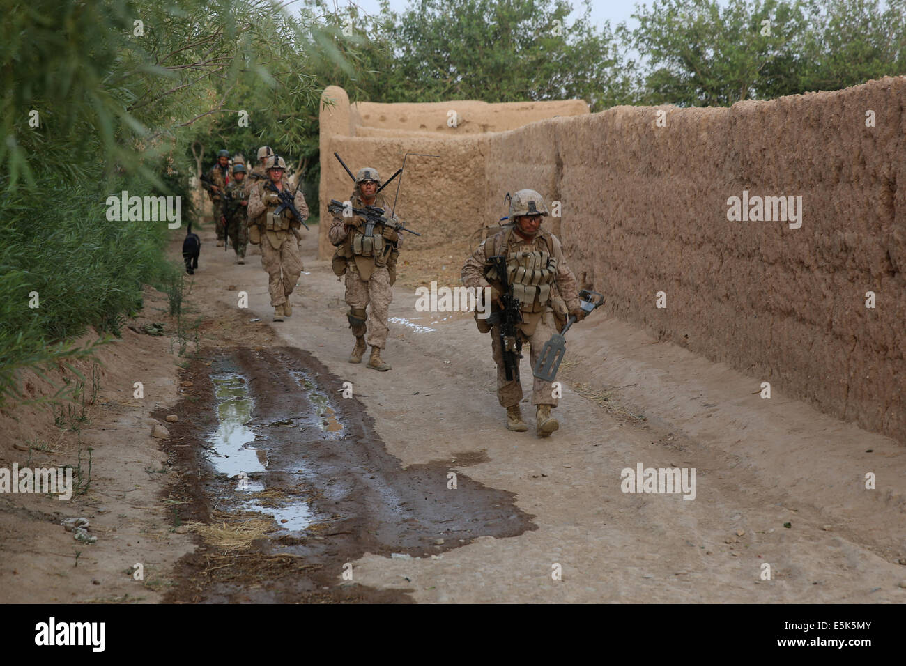 US Marines with the 1st Battalion, 7th Marine Regiment, patrol along a village wall during a mission July 4, 2014 in Gereshk,  Helmand province, Afghanistan. Stock Photo