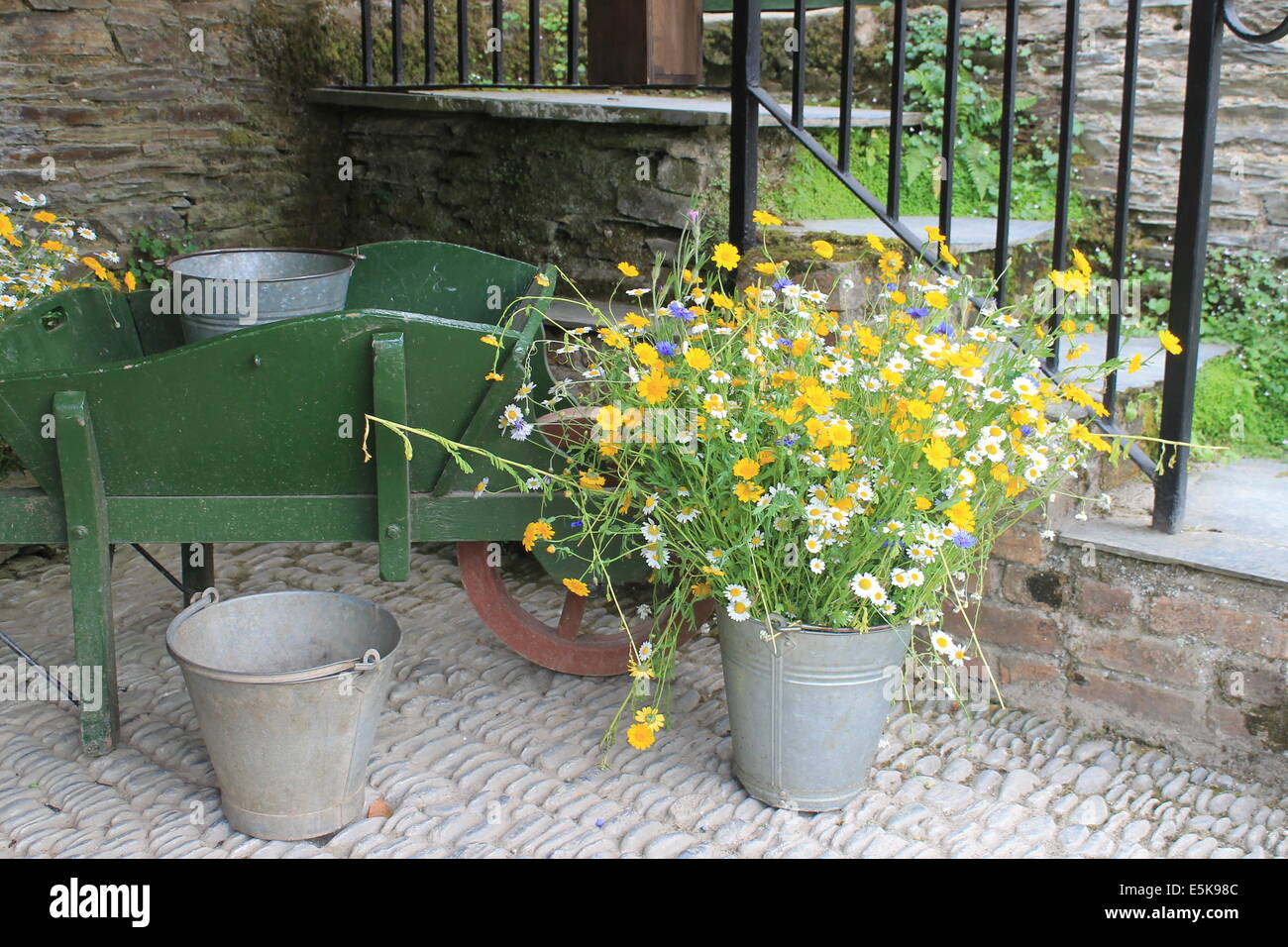 A spray of wildflowers and old wooden wheelbarrow in a courtyard corner at The Lost Gardens of Heligan, Cornwall, England, UK Stock Photo