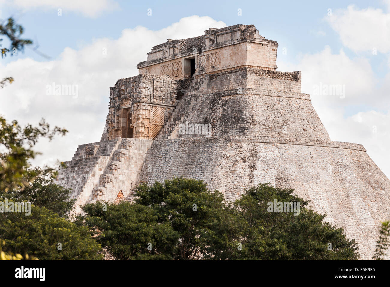 Uxmal's Mayan Pyramid of the Magician rises above the trees. The massive stone structure rises majestically. Stock Photo