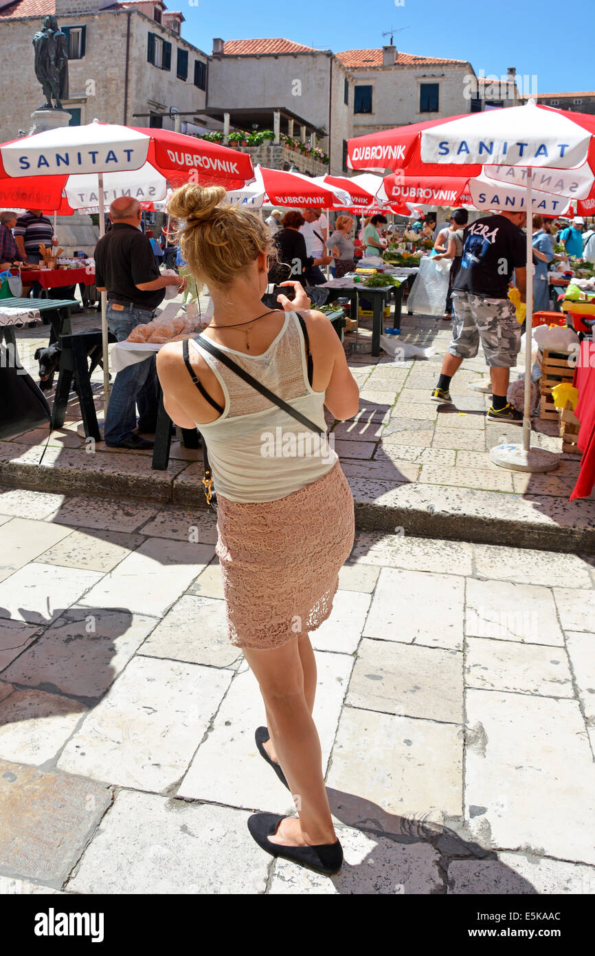 Back view woman tourist person taking photo on mobile phone busy colourful market square stalls & parasol Dubrovnik Croatia Dalmatia Adriatic Europe Stock Photo