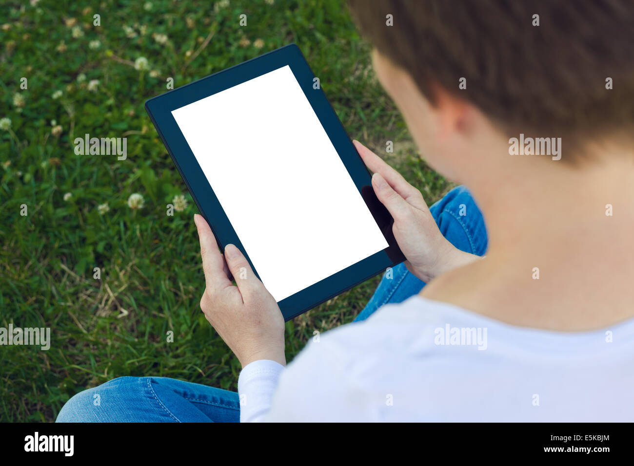 Woman holding digital tablet computer with blank white screen and browsing the internet while sitting on green grass in the park Stock Photo