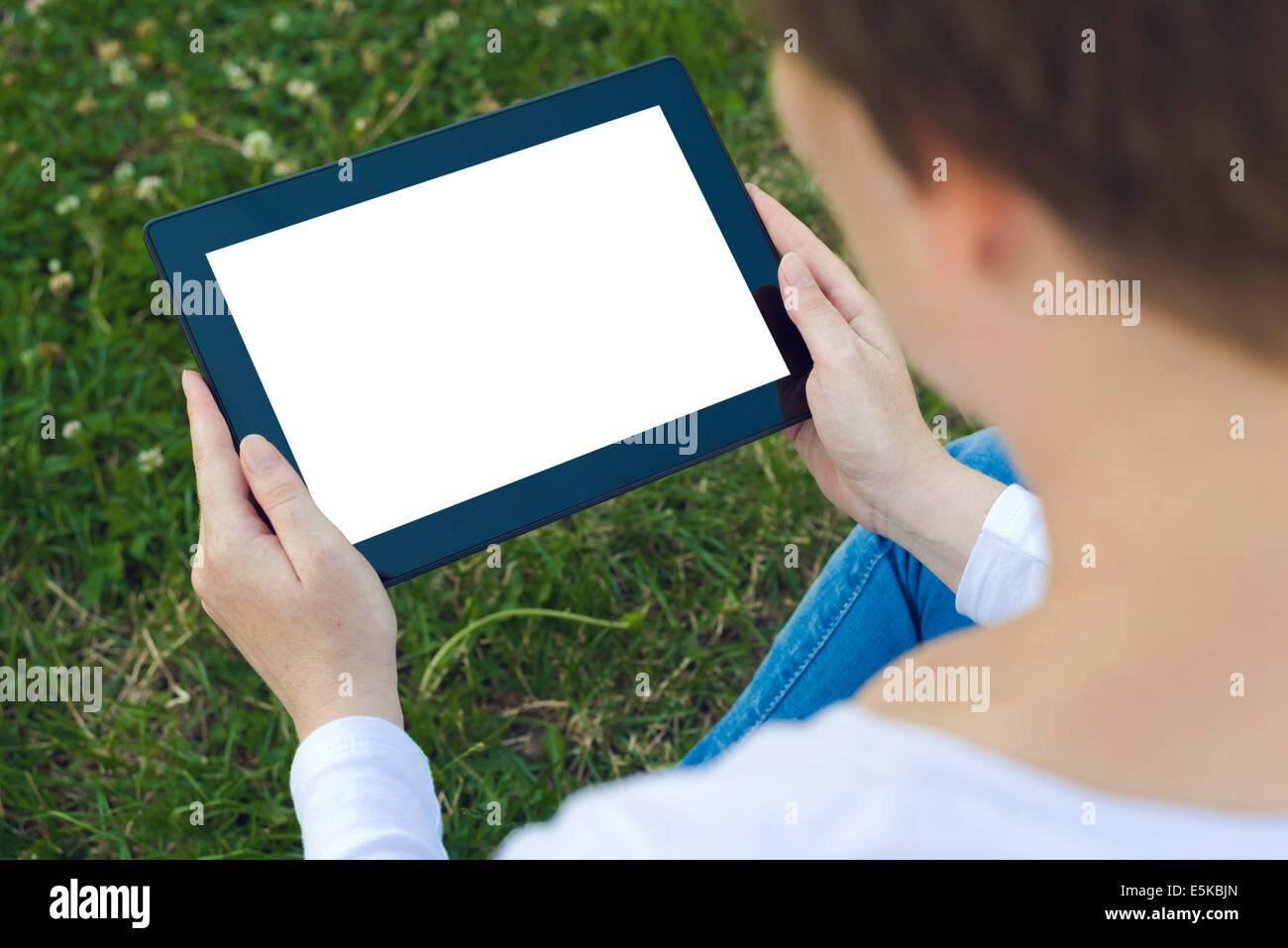 Woman holding digital tablet computer with blank white screen and browsing the internet while sitting on green grass in the park Stock Photo