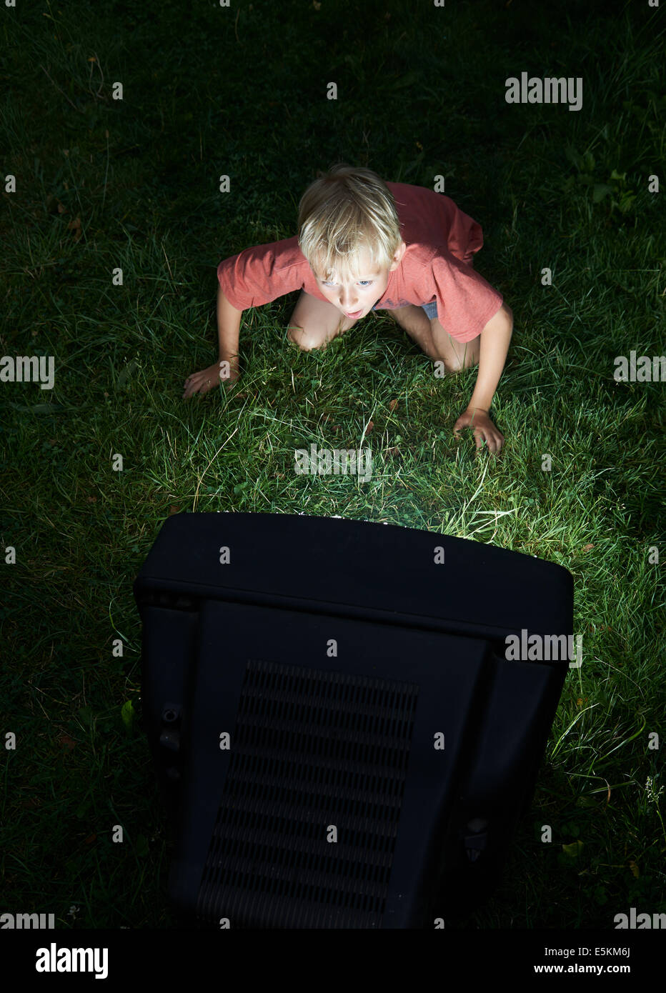 Child Blond Boy Watching Television in Yard, outside in green grass lawn, emotional, facial expression, grimace, grinning Stock Photo