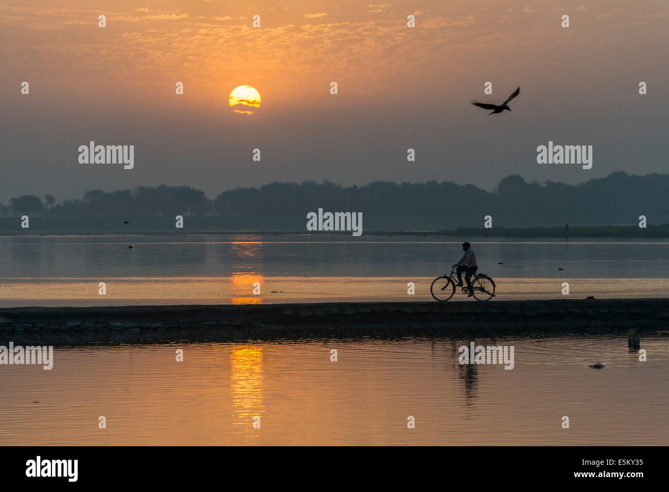 A cyclist crossing the Yamuna river on a dam at sunrise, Vrindavan, Uttar Pradesh, India Stock Photo