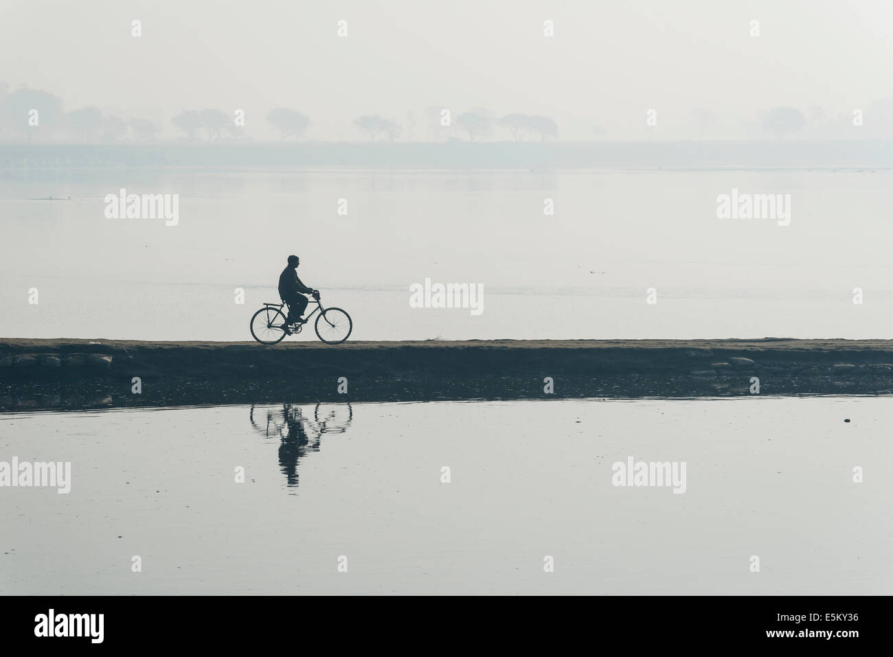 A cyclist crossing the Yamuna river on a dam in the morning haze, Vrindavan, Uttar Pradesh, India Stock Photo