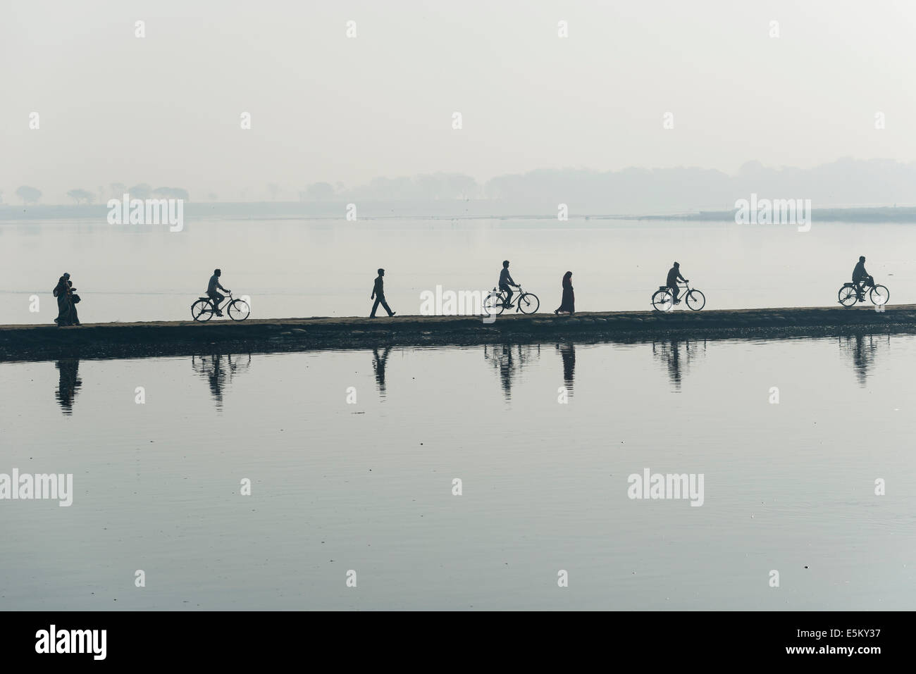 Cyclists and pedestrians crossing the Yamuna river on a dam in the morning, Vrindavan, Uttar Pradesh, India Stock Photo
