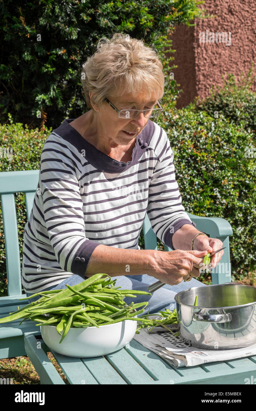 Older woman with rheumatoid arthritis in garden UK slicing home-grown green/runner beans ready for freezing for later use Stock Photo