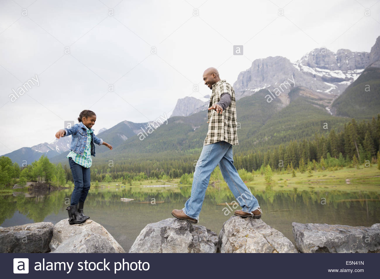 Father and daughter balancing on rocks at lake Stock Photo