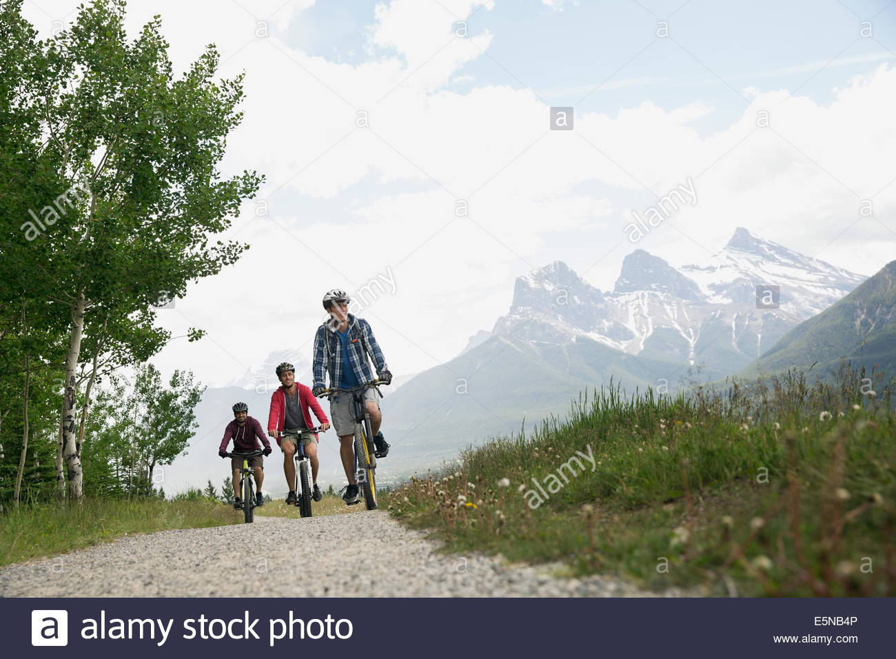 Men mountain biking on trail below mountains Stock Photo