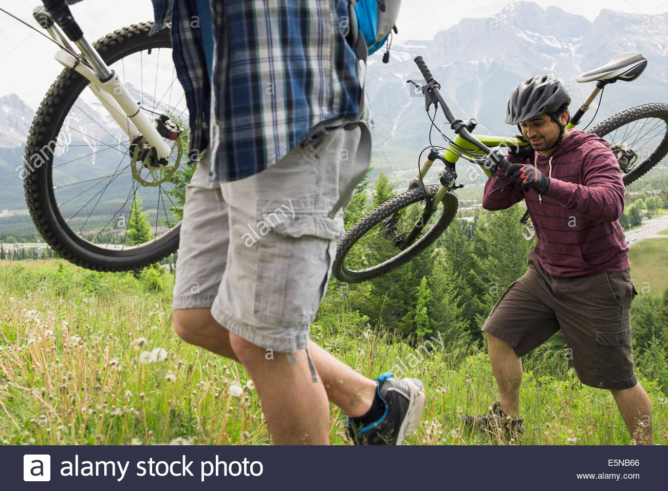 Men carrying mountain bikes up grassy hill Stock Photo Alamy