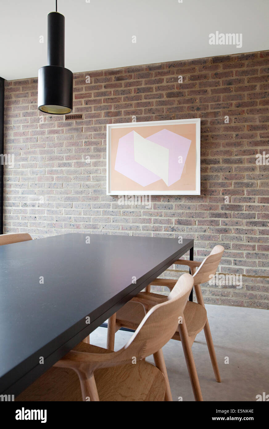 Dining table with modern artwork on exposed brick wall in Duggan Morris house, Kings Grove, Peckham, London, UK. Stock Photo
