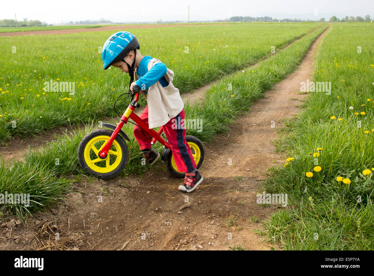 Little boy playing with his bike outdoors with a colourful safety helmet. Stock Photo