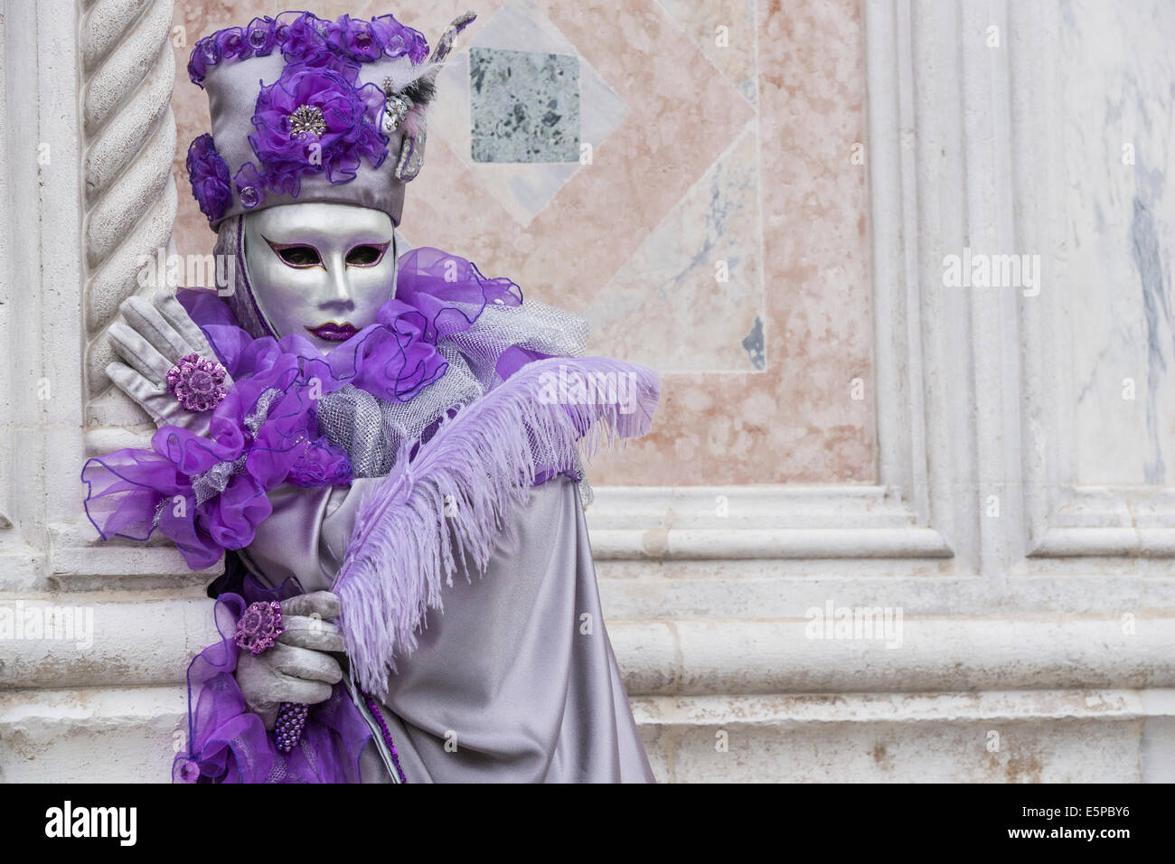 Man in stylized sliver & purple clown costume looks around column of
