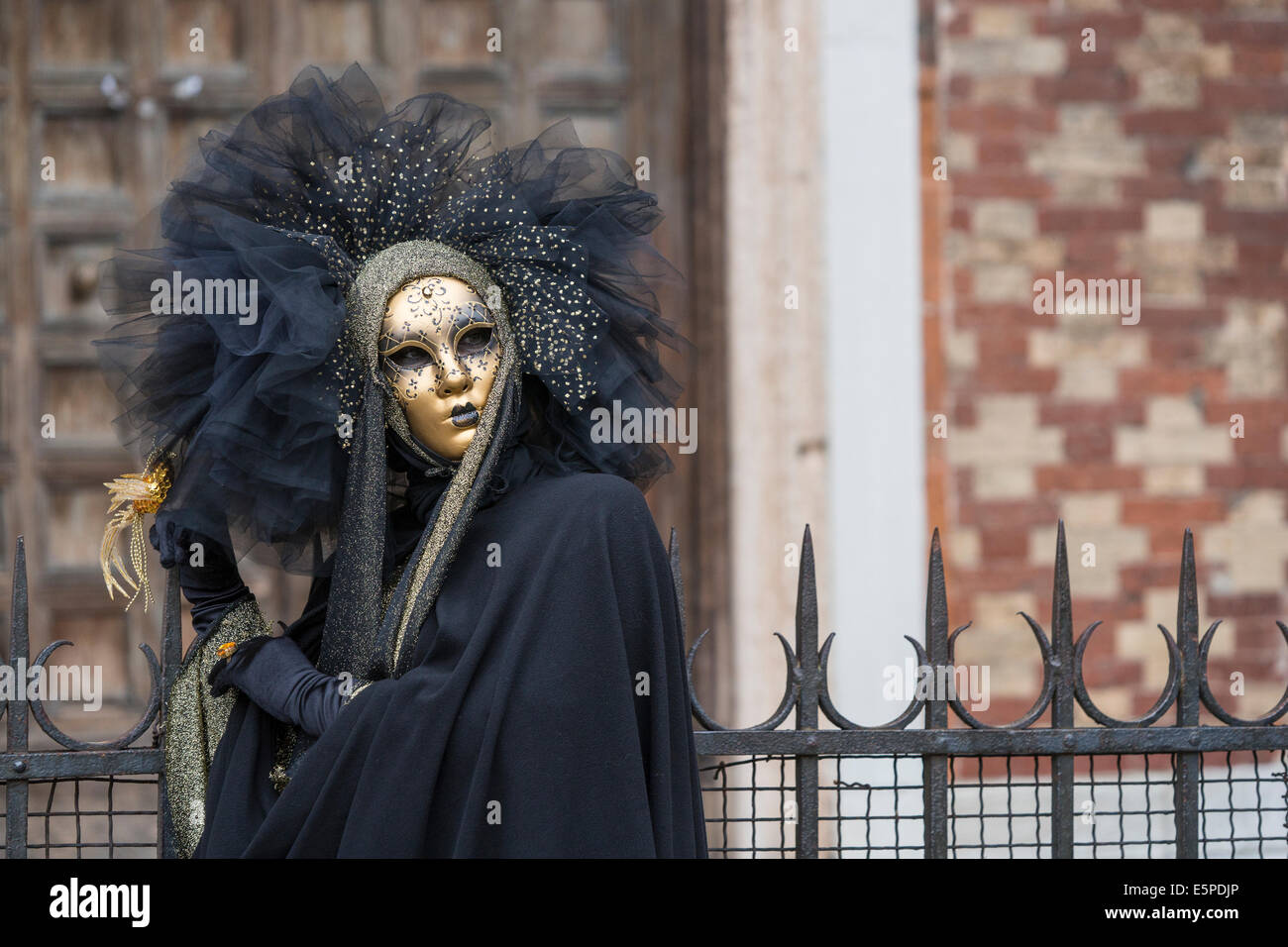 Woman in black costume with gold and lace headdress by San Zaccaria Church during Carnival in Venice. Stock Photo