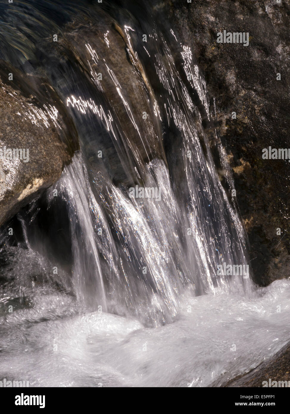 Closeup of small sunlit waterfall in tumbling mountain stream Stock Photo