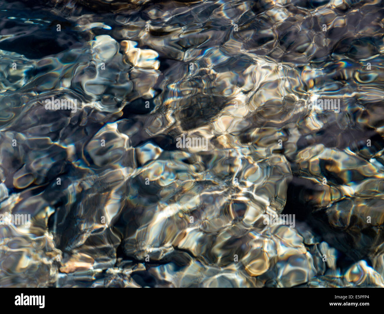 Abstract colourful shallow water ripple patterns above sunlit pebbles in stream bed, Scotland, UK Stock Photo