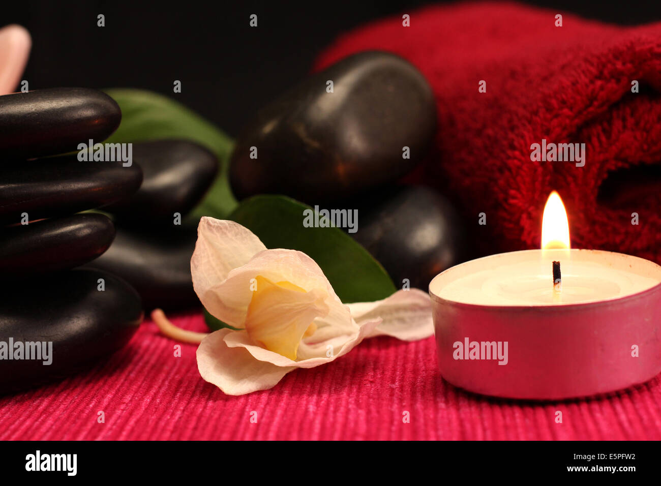 A pile of balanced black spa therapy stones surrounded by candles Stock Photo