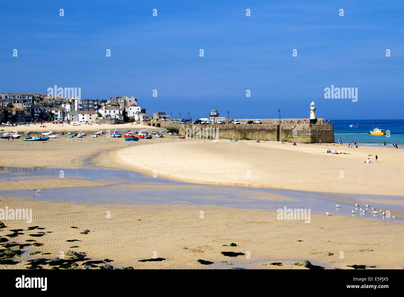 Landscape of St Ives Harbour Cornwall England in low tide showing beach Pier lighthouse town sandbar in bright sunshine Stock Photo