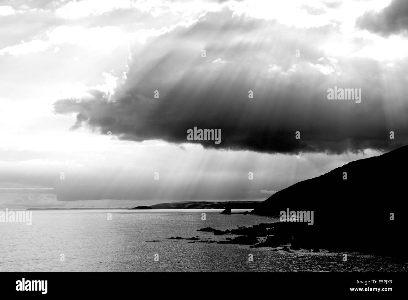 A Black and White seaside image of Portwrinkle  beach Cornwall South West England with stormy clouds and sunrays coming through Stock Photo