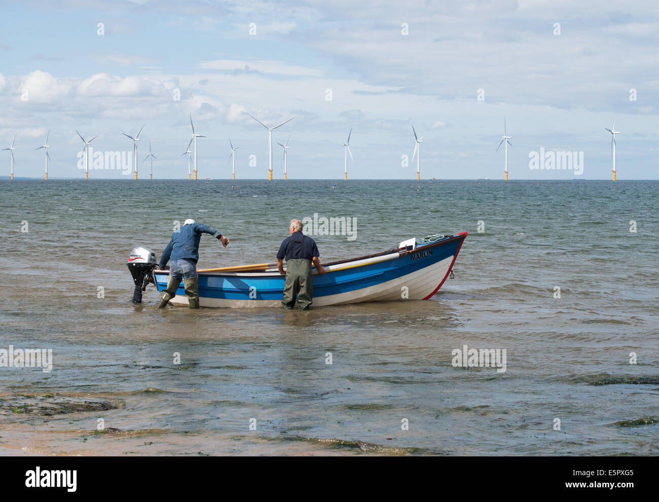 Two fishermen launching a boat with offshore wind farm behind, Redcar, Redcar and Cleveland, England, UK Stock Photo