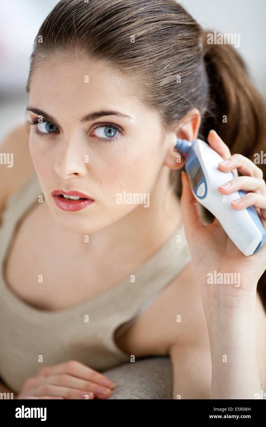 Woman taking her temperature with a digital tympanic thermometer. Stock Photo