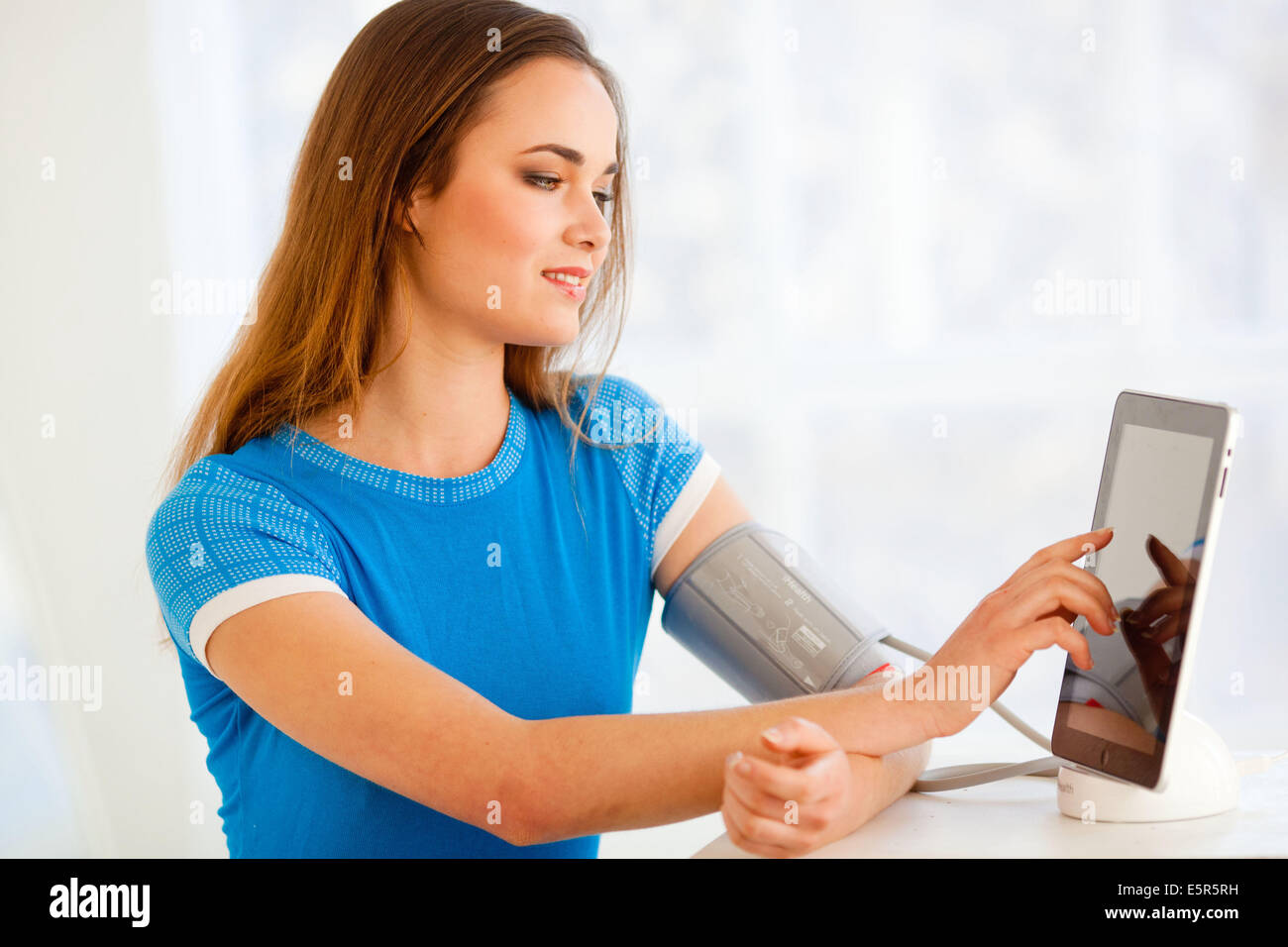 Woman taking her blood pressure with a docking station iPad application iHealth®. Stock Photo